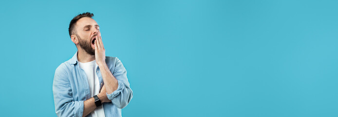 A man stands against a solid blue background, yawning while crossing his arms. He appears relaxed, dressed casually in a light shirt. The scene suggests a lighthearted moment.