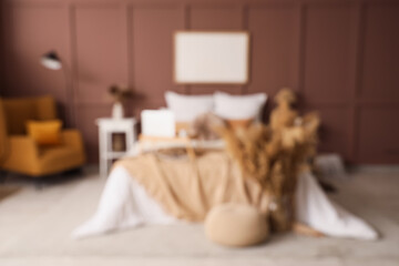 Blurred view of stylish bedroom with cozy bed, bedside table and armchair