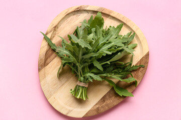Wooden plate with bunch of fresh arugula leaves on pink background