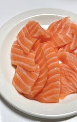 Fresh salmon sashimi arranged neatly on a plate with vibrant orange slices and delicate marbling, accompanied by garnish such as shredded radish and green leaves, creating a visually appealing