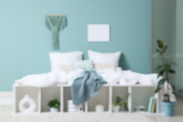 Blurred view of bedroom with big comfortable bed and houseplants near mint wall