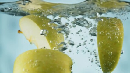 Apple slices falling into water, creating bubbles and splashes against a light blue background, for food advertising