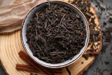 Fototapeta premium Bowl with dry black tea leaves and cinnamon on dark background