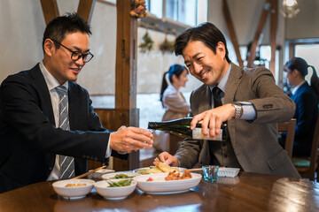 A smiling businessman pouring drinks for his boss or colleague at a bar