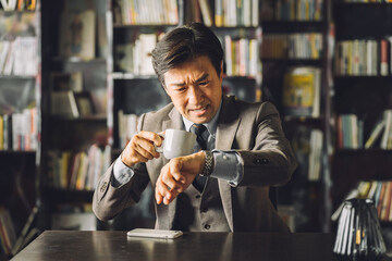 Asian male businessman surprised looking at his watch in the library or study (late, surprised, busy, appointment, schedule)
