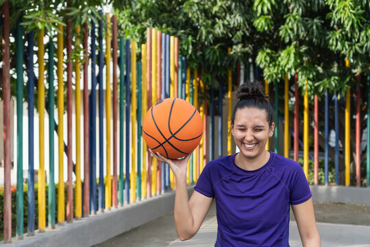 Young woman laughing playing basketball in park