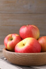 Ripe red apples in bowl on table against wooden background, closeup
