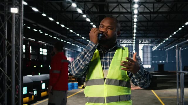 Black engineer talks into walkie talkie and supervising fabrication tools in a workshop, demonstrating strong labor involvement and development for activity within industry plant. Camera A.