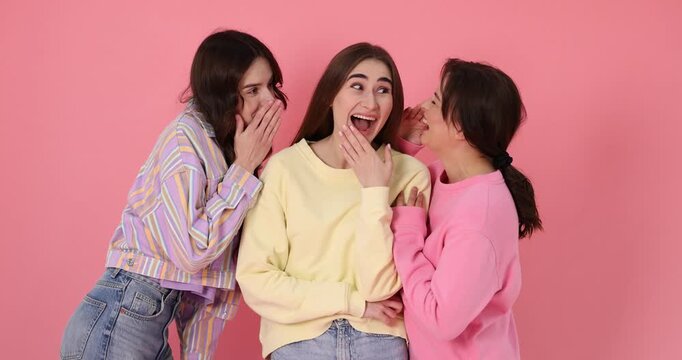 Three friends in stylish clothes gossiping on pink background