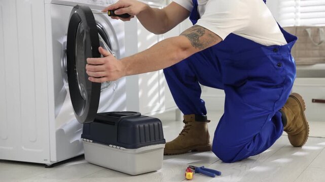 Repairman fixing broken washing machine with screwdriver at home, closeup. Camera moving forward
