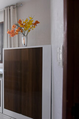modern home cabinet with brown wood doors, metal vase and colorful artificial flowers, interior decoration detail, minimalist home decor with storage unit, white wall and natural light
