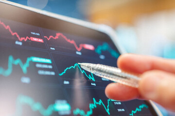 Analyzing stock market data on a tablet screen with a pen pointing at the graph