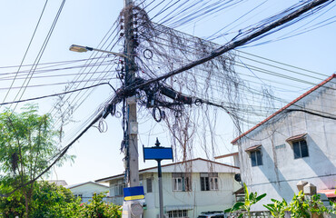 A chaotic and dense cluster of utility wires and cables hangs haphazardly from a concrete utility pole in a suburban setting.