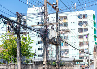 A busy, wide-angle shot captures a cluster of utility poles supporting a large, central electrical transformer and an extremely dense and tangled mass of black wires and cables.