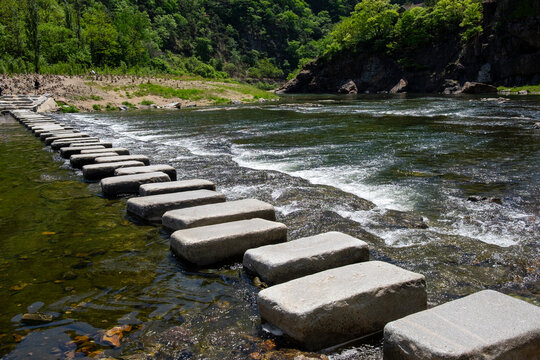 A landscape with a stepping stone bridge and a mountain by the river