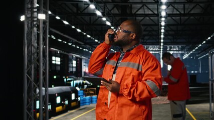 African american professional worker using walkie talkie radio in industry plant, reinforcing communication needed to manage production, fabrication and assembly tasks. Safety vest. Camera A.