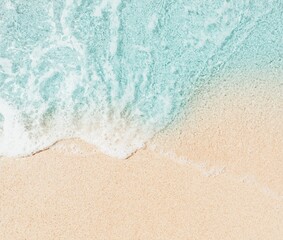 Close-up aerial view of clear, vibrant turquoise sea water with white foam from a gentle wave meeting the fine, light beige sand of a tropical beach. The image a serene and tranquil natural scene. 