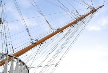Close-up of a ship's mast and rigging against a partly cloudy sky