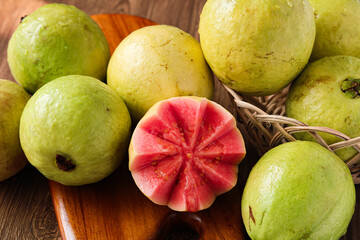 An arrangement of whole green guava fruit, featuring a halved piece that reveals a vibrant pink interior. The flesh is artfully carved to emphasize its texture and color.