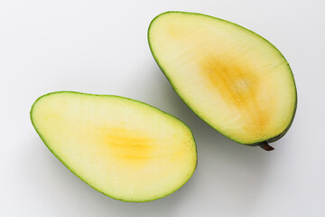 A whole Kiojay mango freshly cut in half, showing its pale yellow flesh against a smooth green skin, set on a clean white background.