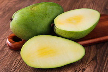A large, firm Kiojay mango is presented whole and halved, showcasing the smooth green skin and pale yellow-white flesh. Often enjoyed in both ripe and unripe preparations.