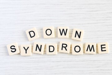 Close up shot of some plastic letter blocks spelling "Down Syndrome" in English on white wooden background.