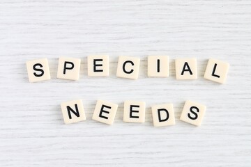 Close up shot of some plastic letter blocks spelling "Special Needs" in English on white wooden background.