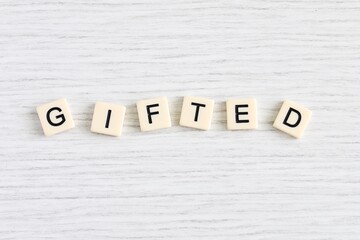 Close up shot of some plastic letter blocks spelling "Gifted" in English on white wooden background.