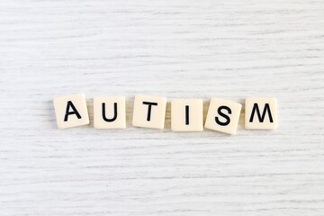 Close up shot of some plastic letter blocks spelling "Autism" in English on white wooden background.