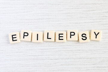 Close up shot of some plastic letter blocks spelling "Epilepsy" in English on white wooden background.