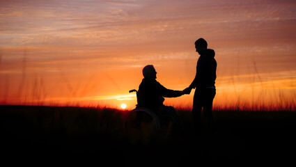 Couple holding hands at sunset one person in a wheelchair