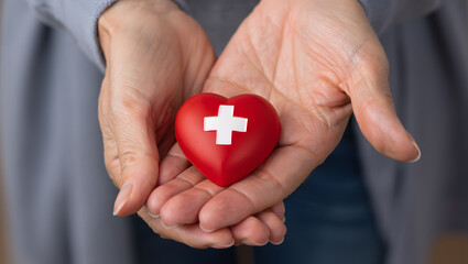 Hands holding a red heart with a white cross symbolizing health and care