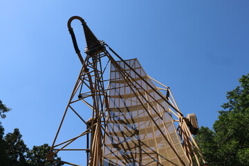 A low-angle shot of a dish antenna of military radar, set against a clear blue sky and framed by green treetops.