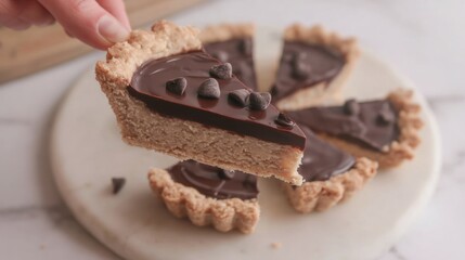 A delicious slice of chocolate tart held by hand, showcasing a rich chocolate filling and a crumbly crust, with chocolate chips on top.
