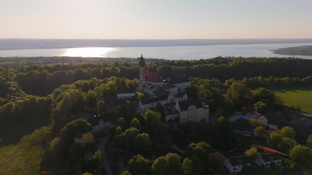 Luftaufnahme Kloster Andechs bei Muuenchen, Bayern. Drohnenvideo Wallfahrtskirche auf dem Heiligen Berg am Ammersee mit Landschaft, See und Sonnenuntergang. Burg Andechs. Braustuberl des Klosters. 
