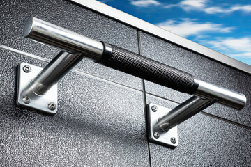 A close-up of a metallic pull-up bar attached to a textured wall, highlighting its grip and sleek design against a backdrop of blue sky.