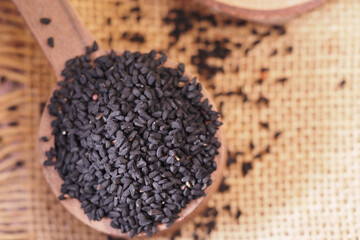 black cumin seed are piled in a wooden spoon on a textured surface
