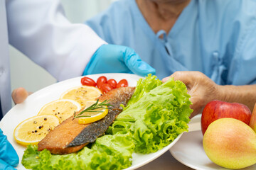 Asian elderly woman patient eating salmon stake and vegetable salad for healthy food in hospital.