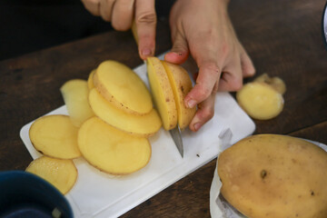 Closeup of person hand slicing fresh potato with mandoline in kitchen. This food preparation for cooking healthy vegetable meal shows careful, domestic skill
