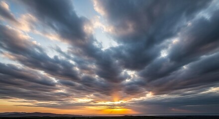 Dramatic and vibrant sunset or sunrise sky with dark, textured clouds stretching across the horizon, showcasing a beautiful interplay of light and shadow as the suns rays break through the cloud cover