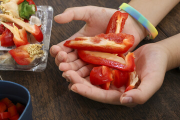 Careful child hand holding fresh red pepper slice. kid preparing food with vegetable ingredient in domestic kitchen. healthy meal preparation for nutritional diet
