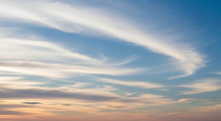 Obraz premium Expansive blue sky with delicate, elongated white clouds gracefully sweeping across the frame, hinting at a beautiful sunset or sunrise on the horizon