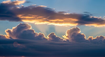Golden light illuminates dramatic clouds in a vibrant sky at sunset or sunrise, creating a breathtaking natural scene with rays of light breaking through