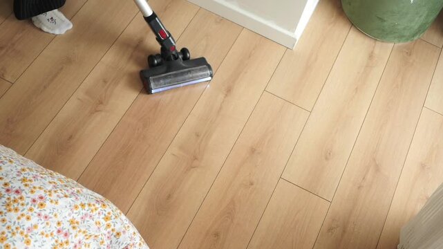 Cleaning hardwood floors with a vacuum in a bedroom