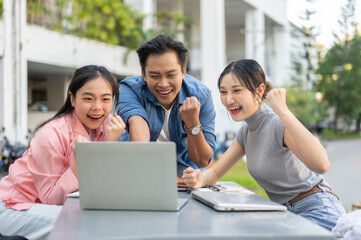 Fototapeta premium Asian woman student making a fist with man and friend while looking at laptop on table in university