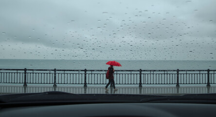 A person with a red umbrella walks alone through a rainy day creating a quiet and contemplative moment