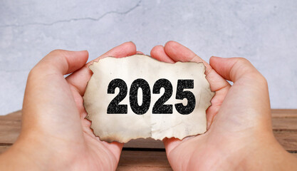A hand holding a vintage burnt piece of paper with the number 2025 printed in a charcoal texture effect. Represents the end of the year, time passing, and change. Concept for the end of 2025
