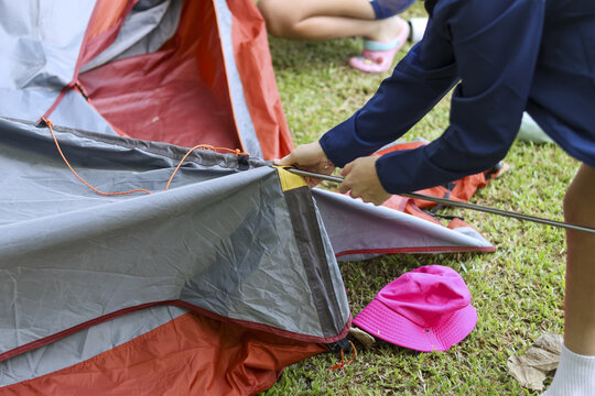 Young child with focus pitching tent for family camping adventure. close up of hand setting up camp equipment on green grass for an outdoor summer activity