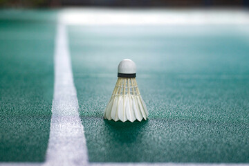 A white shuttlecock sits perfectly on the left side white service lines, sharply contrasting with...