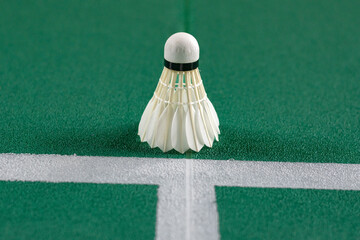 A white shuttlecock sits perfectly on the intersection of the two white service lines, sharply contrasting with the deep green texture of the badminton court surface.